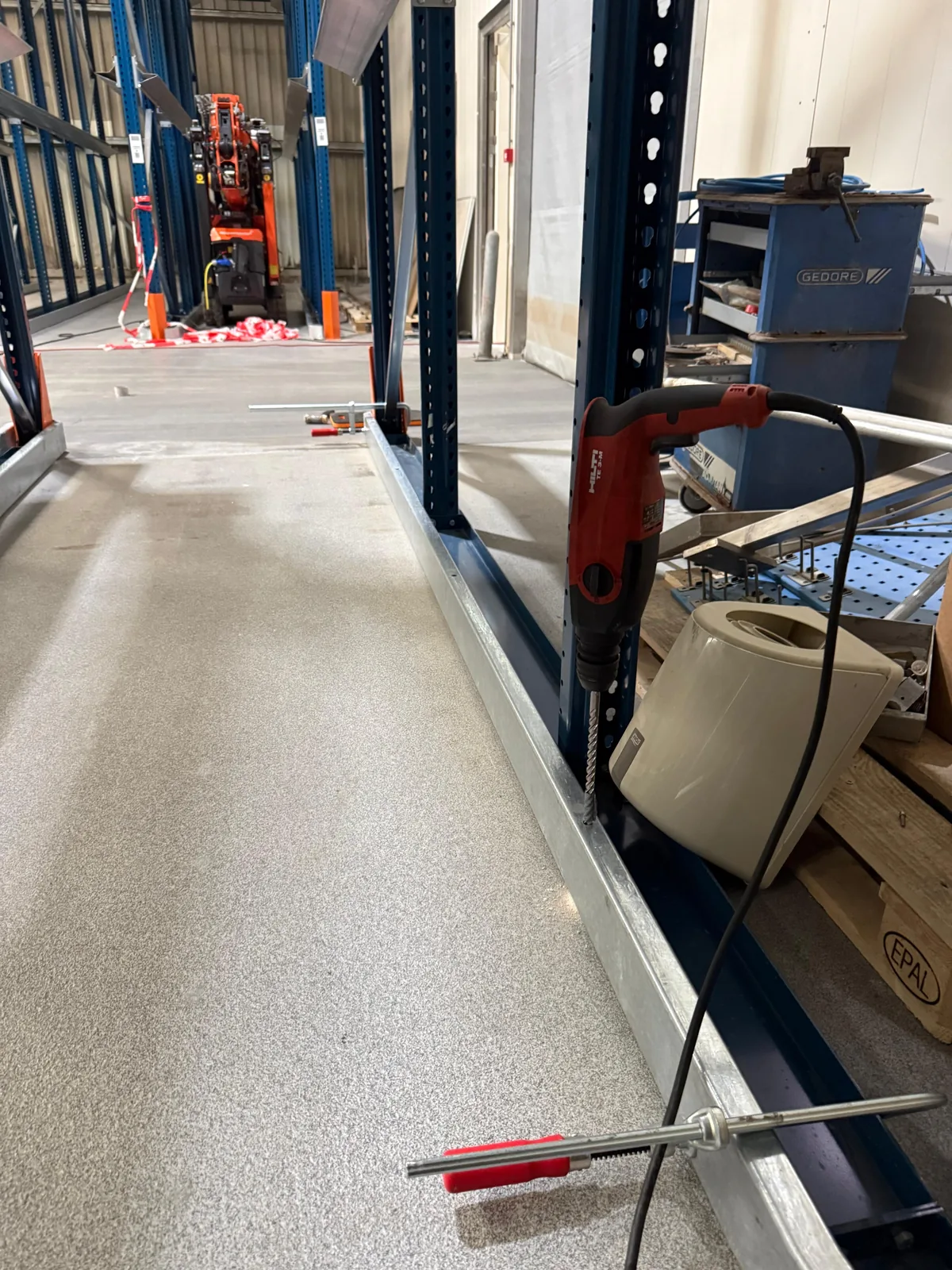 Boorhamer met SDS-boor boort een ankergat van 12 mm in de betonvloer langs de stellingvoet &mdash; Tiel