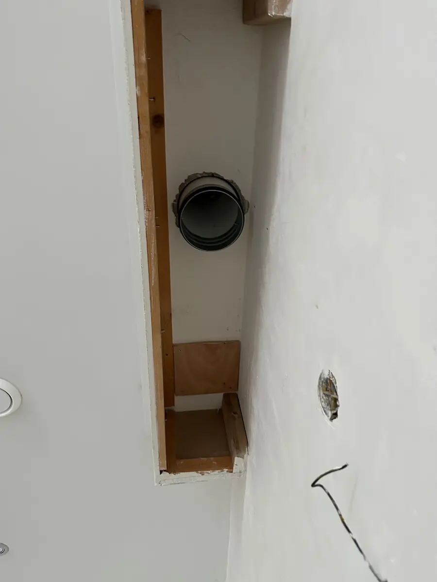 Afzuigkap gat boren Etten-Leur &mdash; Zwarte afvoerbuis van een afzuigkap in een houten opening voor een koof