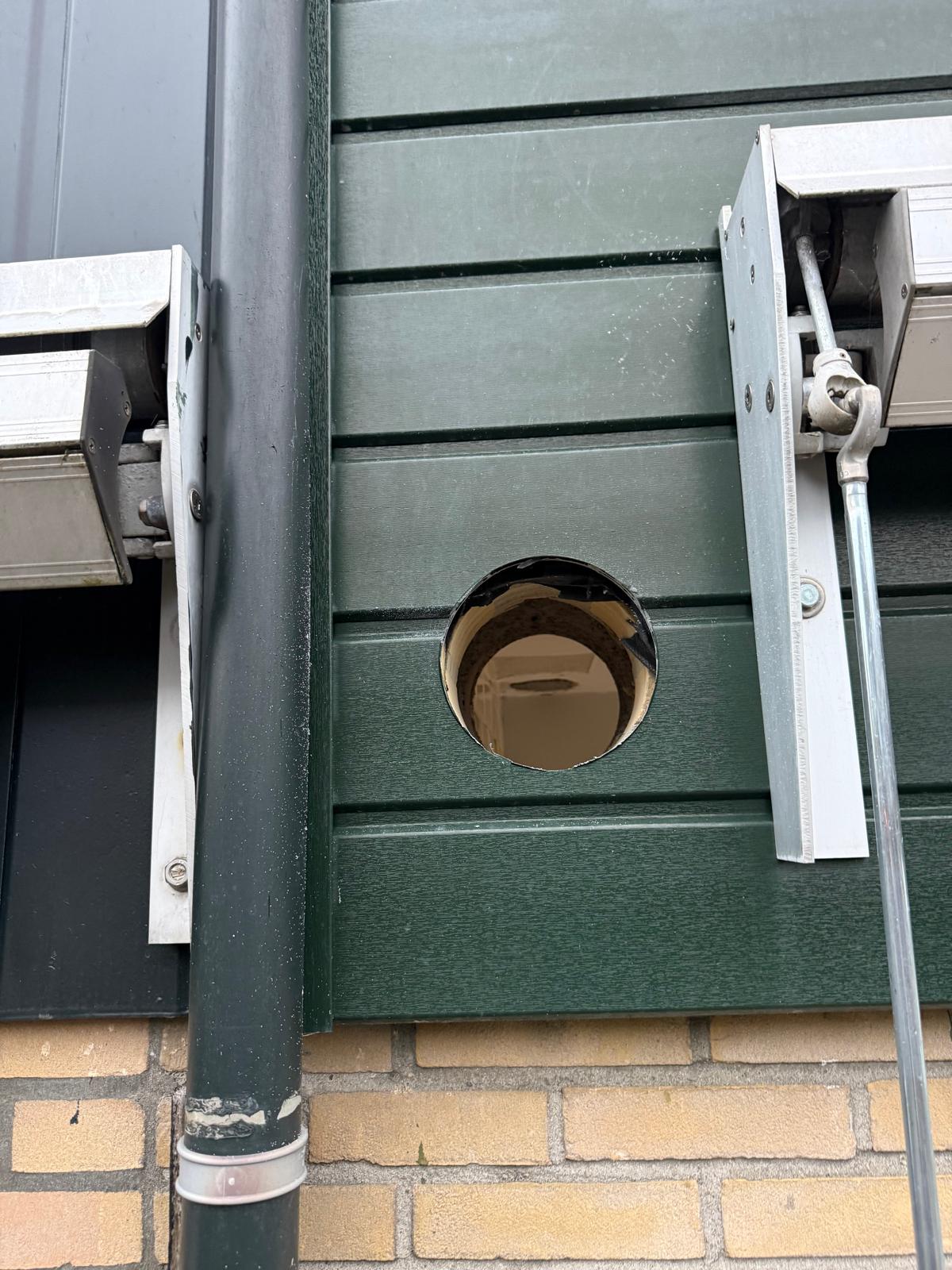 Afzuigkap gat geboord in groene PVC gevelbekleding buiten
