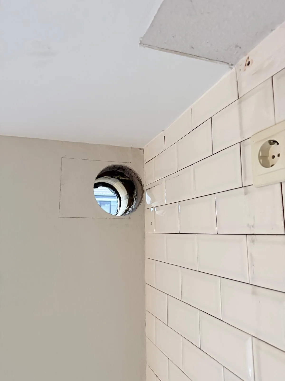 Afzuigkap gat in witte betegelde keukenmuur hoog bij plafond