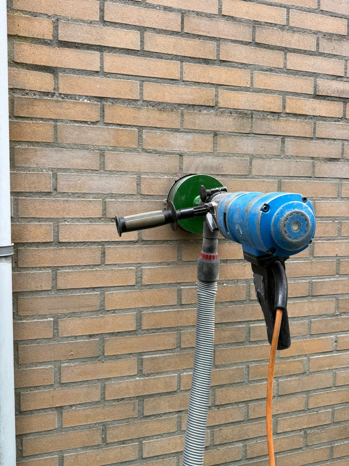 Diamantboorkroon overboort het bestaande afzuigkap gat in de bakstenen buitenmuur — droog geboord met stofafzuiging in Eindhoven