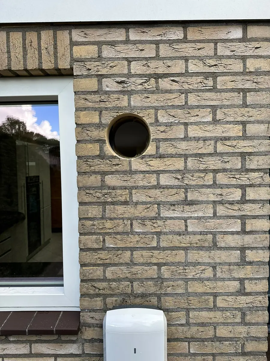 Afzuigkap gat boren Roosendaal &mdash; Afzuigkapgat in een beige-gele bakstenen gevel, naast een wit kozijn