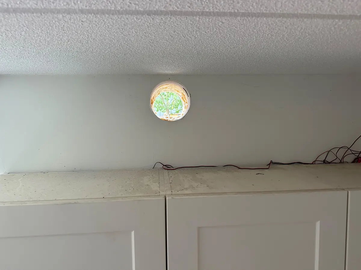 Vers geboord afzuigkapgat boven de keukenkastjes, met daglicht door de opening