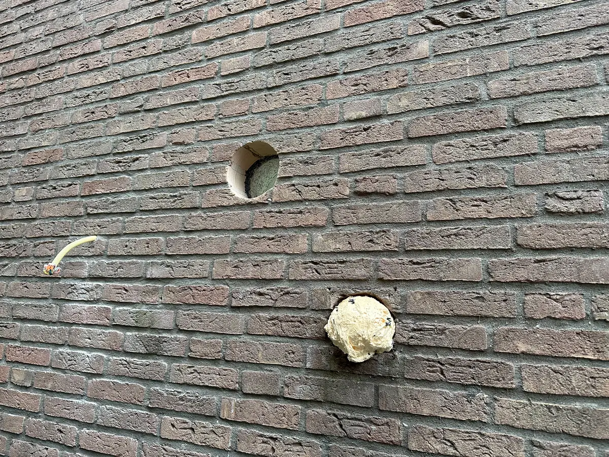 Afzuigkap gat boren Groningen &mdash; Nieuw afzuigkapgat in donkerrode baksteen, boven een oude opening die met pur is dichtgezet