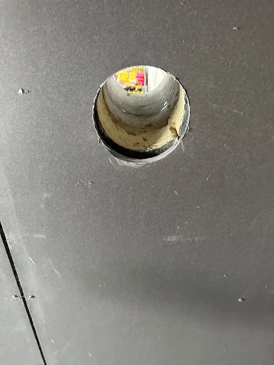 Afzuigkap gat boren Middelburg &mdash; Afzuigkapgat door een grijze gevelplaat, met de doorvoer en isolatie zichtbaar in de opening