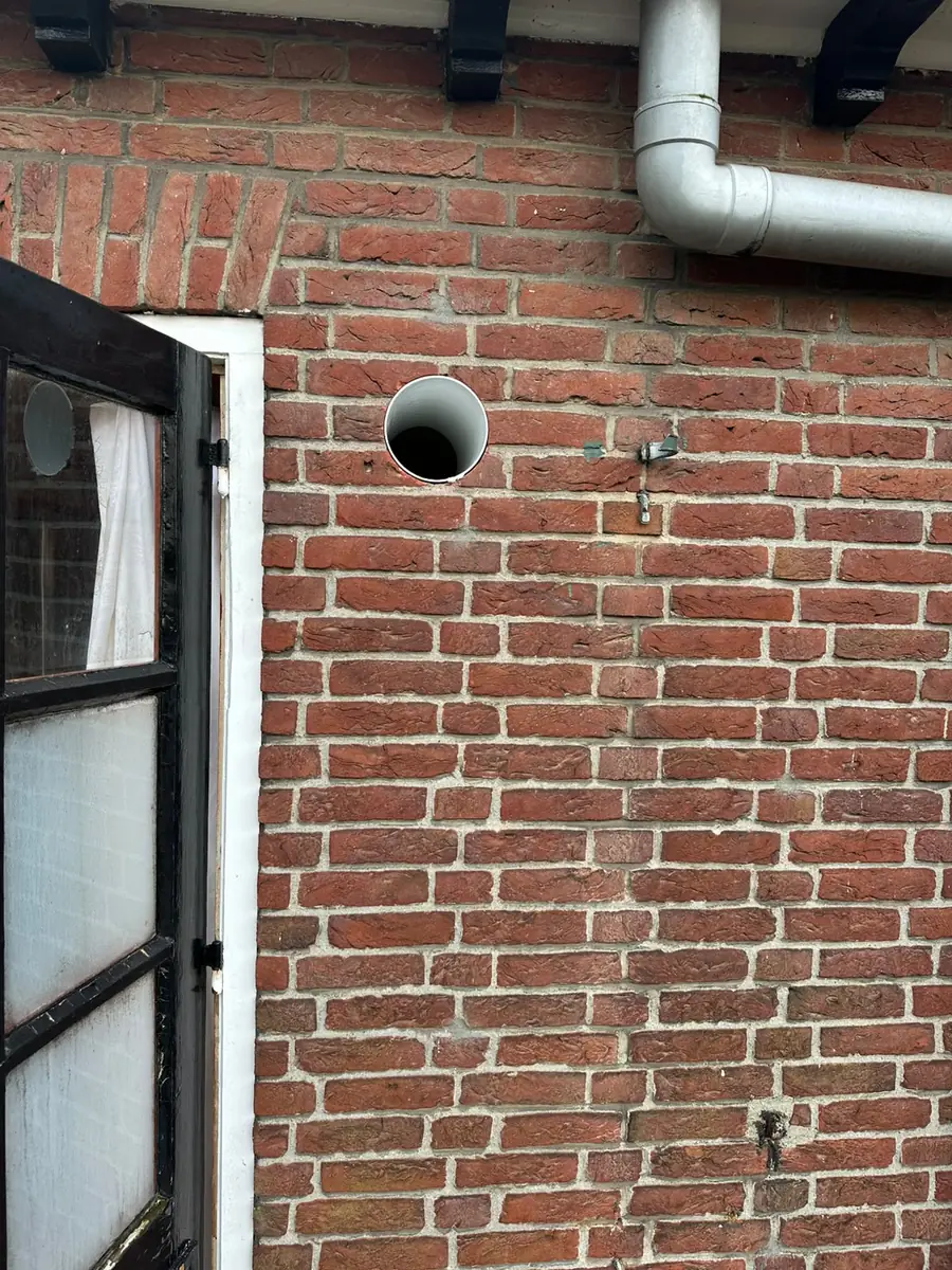 Afzuigkap gat boren Waalwijk &mdash; Afzuigkapgat met witte doorvoerbuis naast een achterdeur, onder de regenpijp