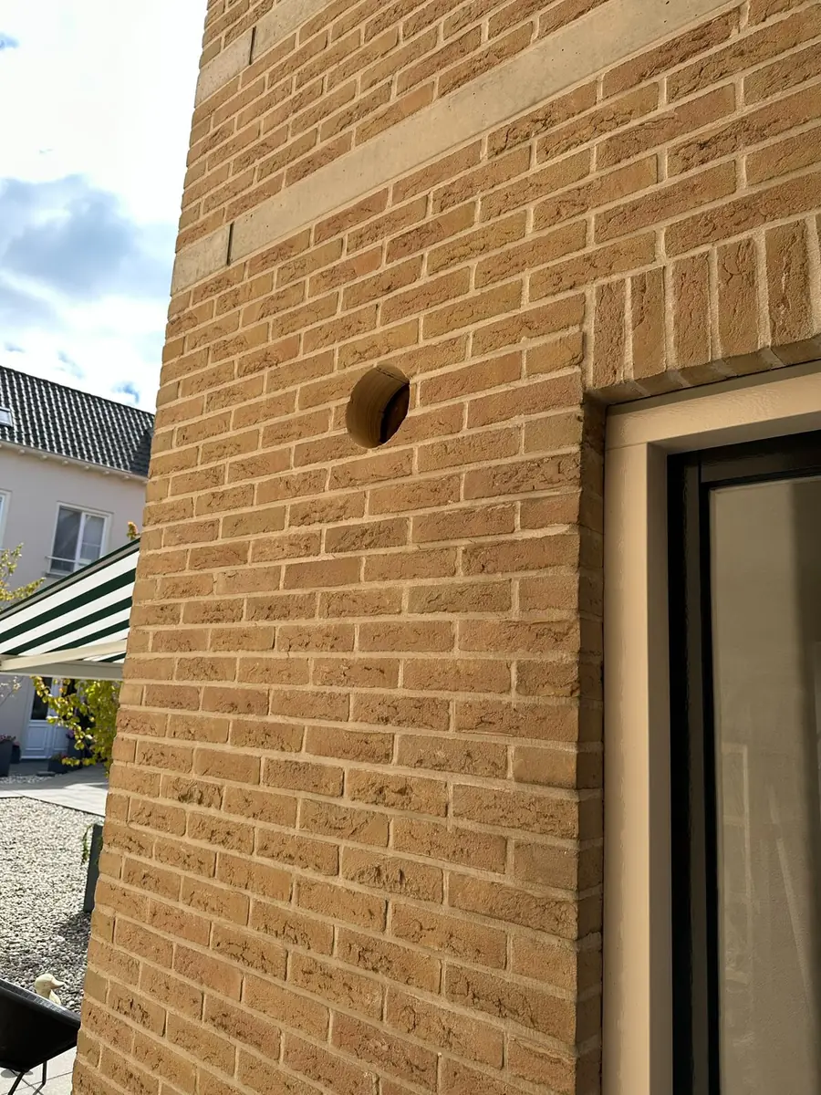 Afzuigkap gat boren Breda &mdash; Afzuigkapgat in de geel-beige bakstenen gevel van een uitbouw, vlak naast het raamkozijn