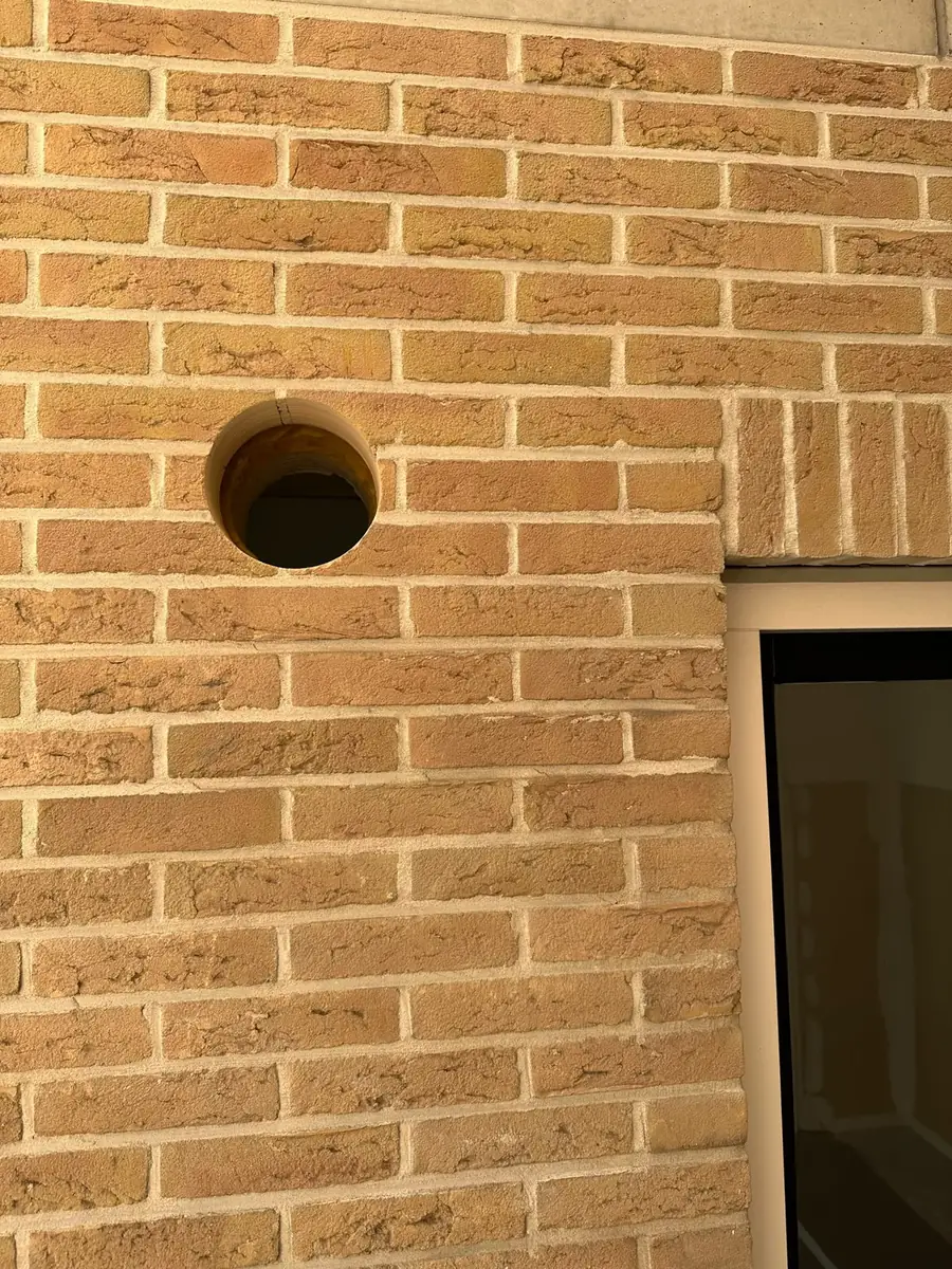 Afzuigkap gat boren Breda &mdash; Close-up van het afzuigkapgat in geel-beige verblendsteen: strakke rand, spouw zichtbaar