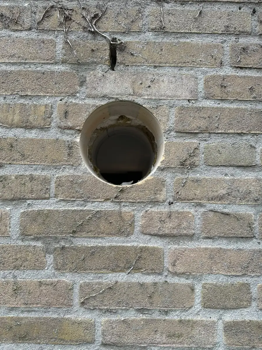 Afzuigkap gat boren Roosendaal &mdash; Close-up van een afzuigkapgat in grijs-beige baksteen: strakke rand, spouw zichtbaar