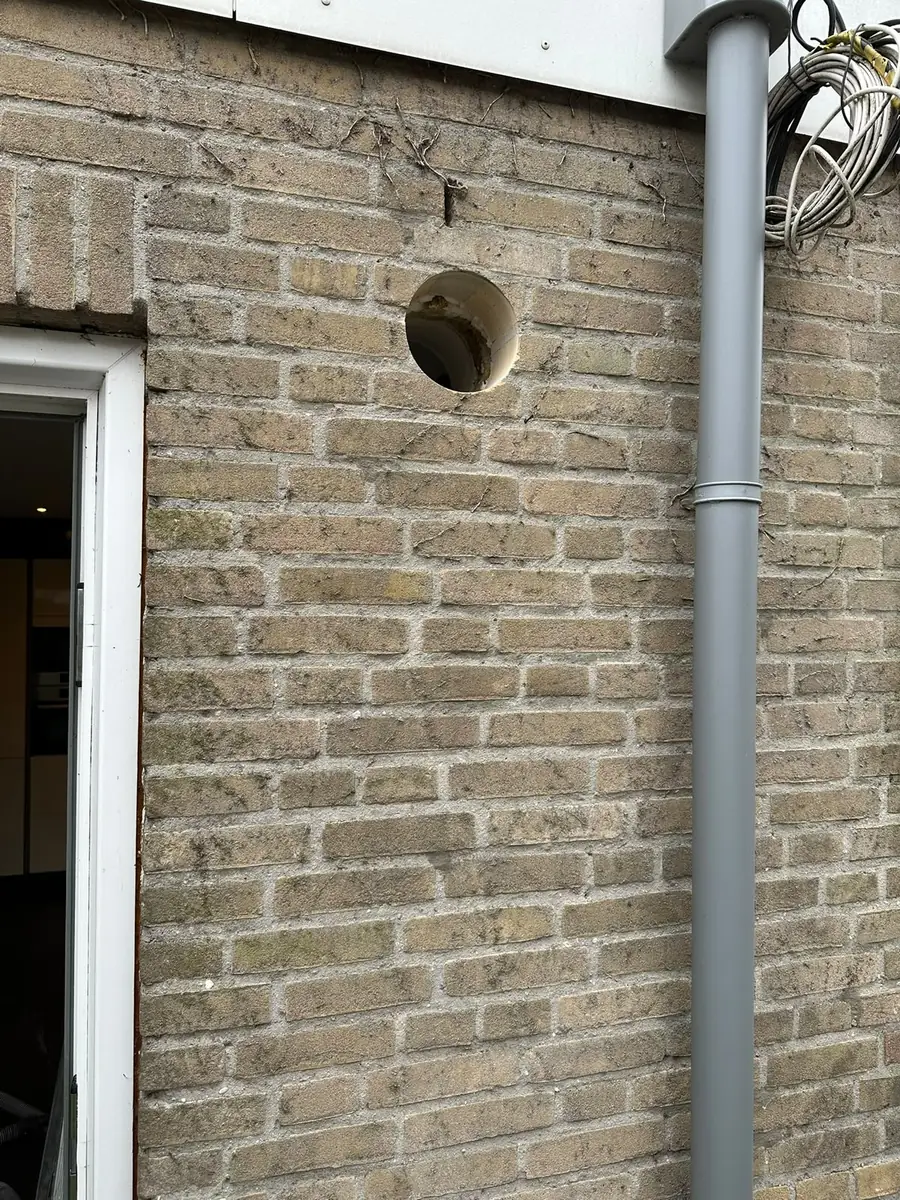 Afzuigkap gat boren Land van Cuijk &mdash; Afzuigkapgat in grijs-beige steen naast een achterdeur en een regenpijp