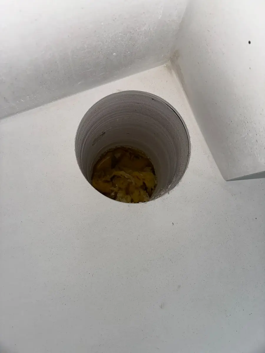 Afzuigkap gat boren Heusden &mdash; Afzuigkapgat hoog in een hoek, met in de spouw de gele isolatie zichtbaar