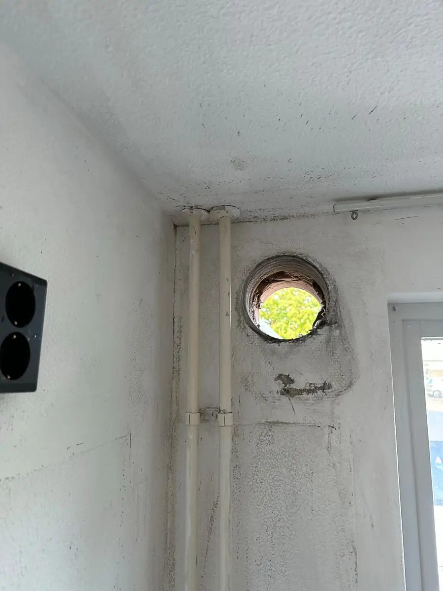 Afzuigkap gat boren Heusden &mdash; Afzuigkapgat in een hoek naast verticale leidingen, met daglicht door het gat