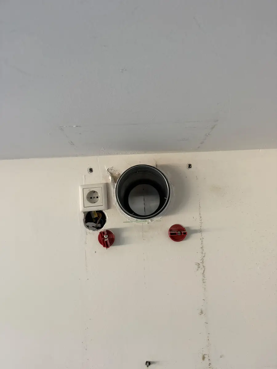 Afzuigkap gat boren Kerkrade &mdash; Metalen doorvoerstuk in het afzuigkapgat vlak onder het plafond, naast een stopcontact