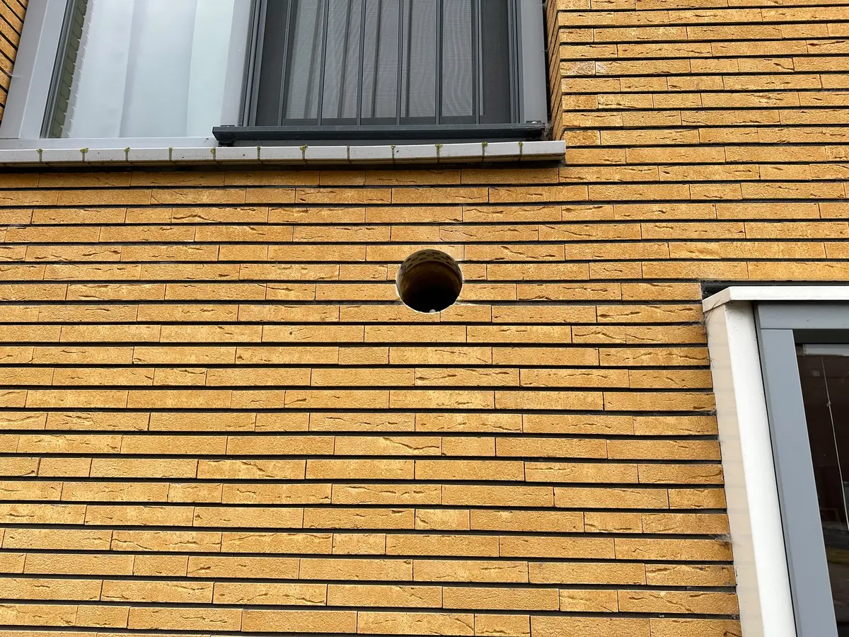Afzuigkap gat boren Oss &mdash; Afzuigkapgat onder een raam in een gevel van okergele, lange en dunne stenen
