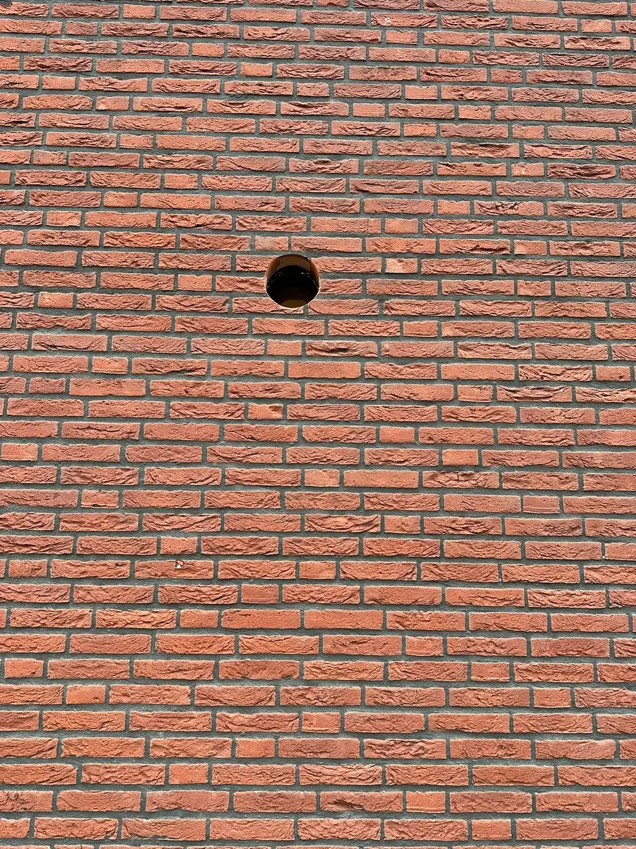 Afzuigkap gat boren Roermond &mdash; Rond afzuigkapgat midden in een gevel van oranjerode baksteen