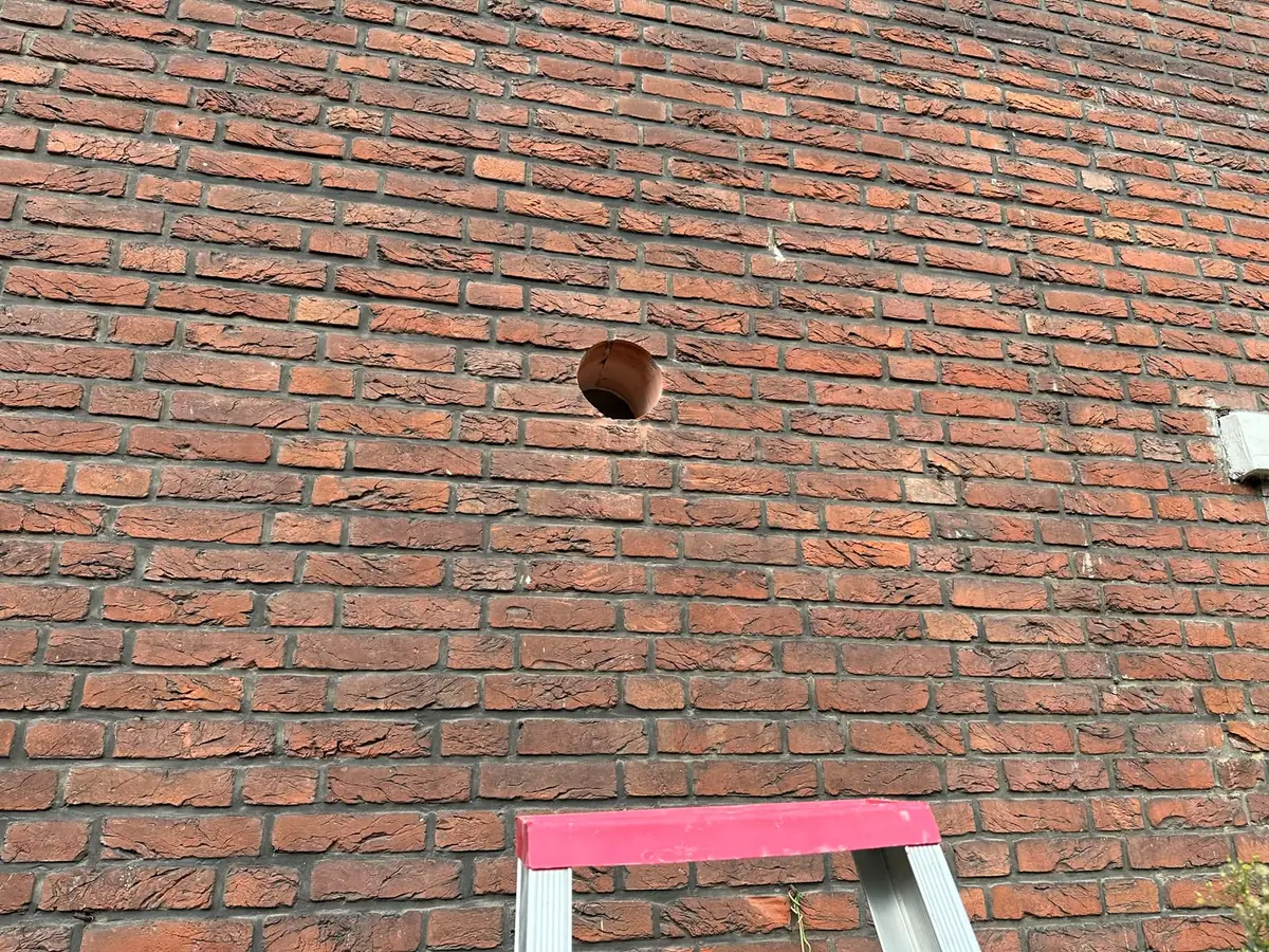 Afzuigkap gat boren Waalwijk &mdash; Vers afzuigkapgat in een oude rode bakstenen gevel, met de ladder eronder