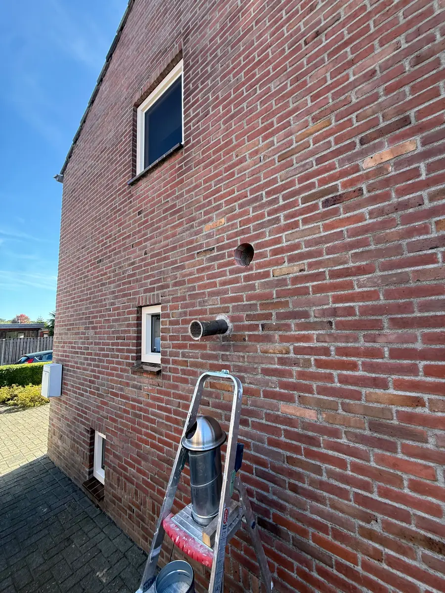 Afzuigkap gat boren Helmond &mdash; Zijgevel van verweerde rode baksteen met een nieuw afzuigkapgat boven een bestaande doorvoer