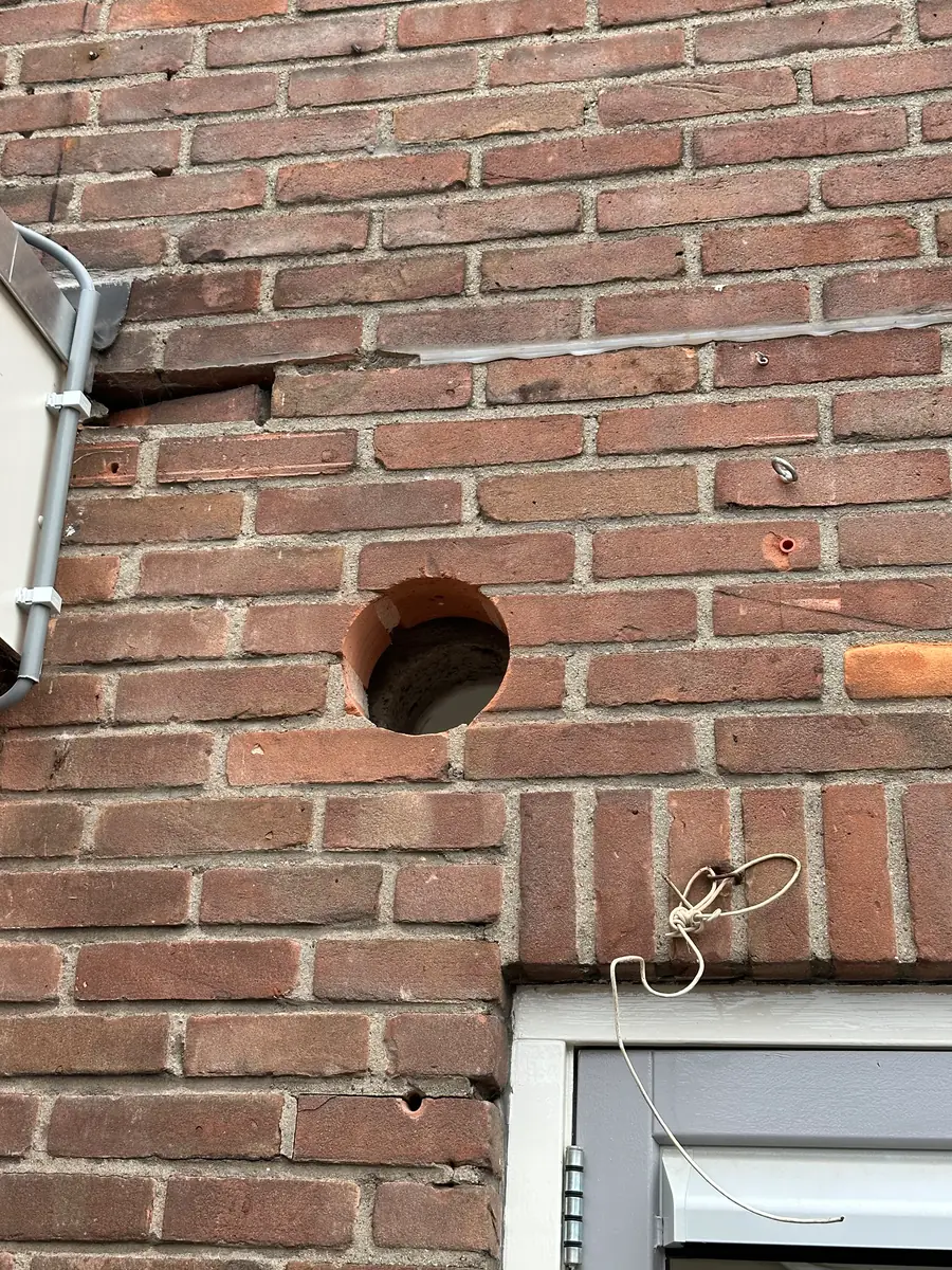 Afzuigkap gat boren Horst aan de Maas &mdash; Afzuigkapgat in rode baksteen boven een deur, naast een oude kabel en een beugel