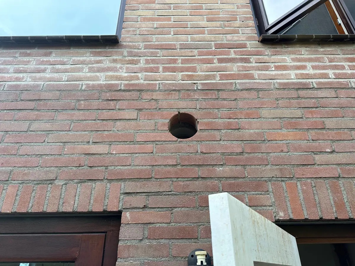 Vers geboord afzuigkapgat in een bakstenen gevel tussen twee ramen