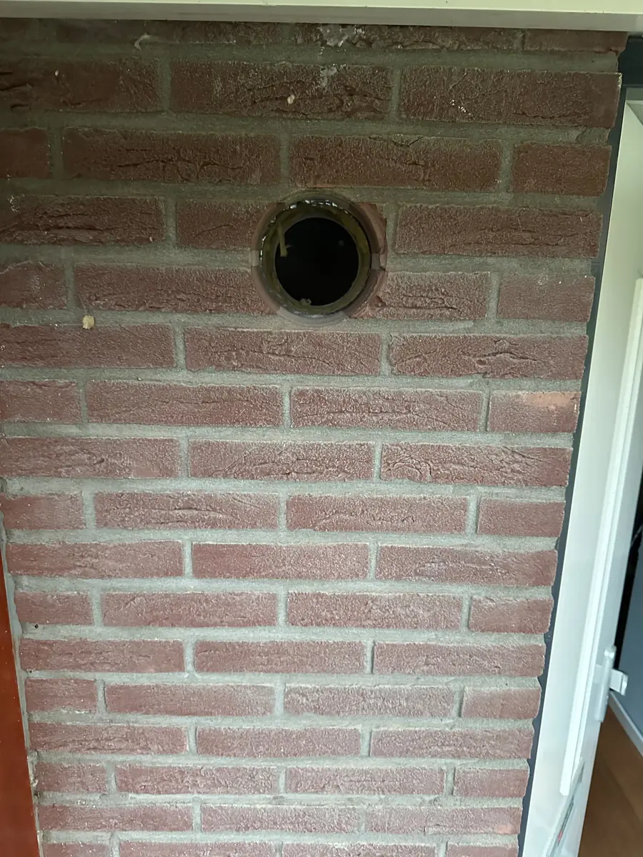 Afzuigkap gat boren Leeuwarden &mdash; Afzuigkapgat met een zwarte ring in een smalle rode bakstenen penant naast een deur