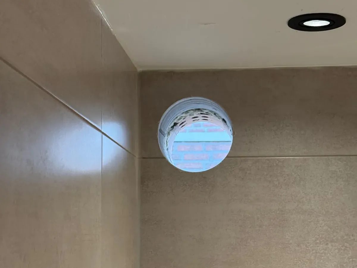 Rond ventilatiegat door de tegelwand van een badkamer, vlak onder het plafond