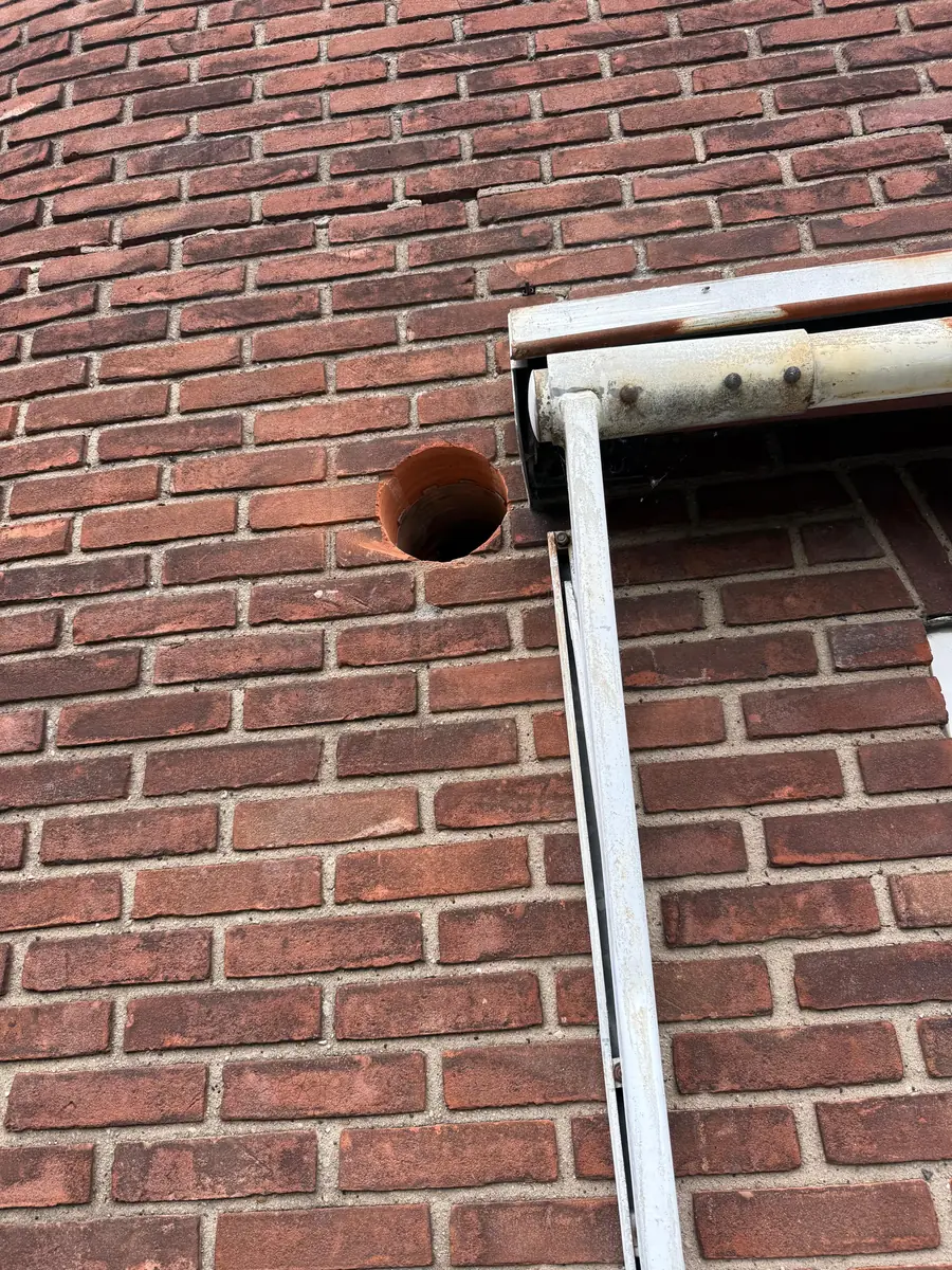 Betonboringen Maasgouw &mdash; ronde doorvoer bovenin de gevel, naast de regenpijp