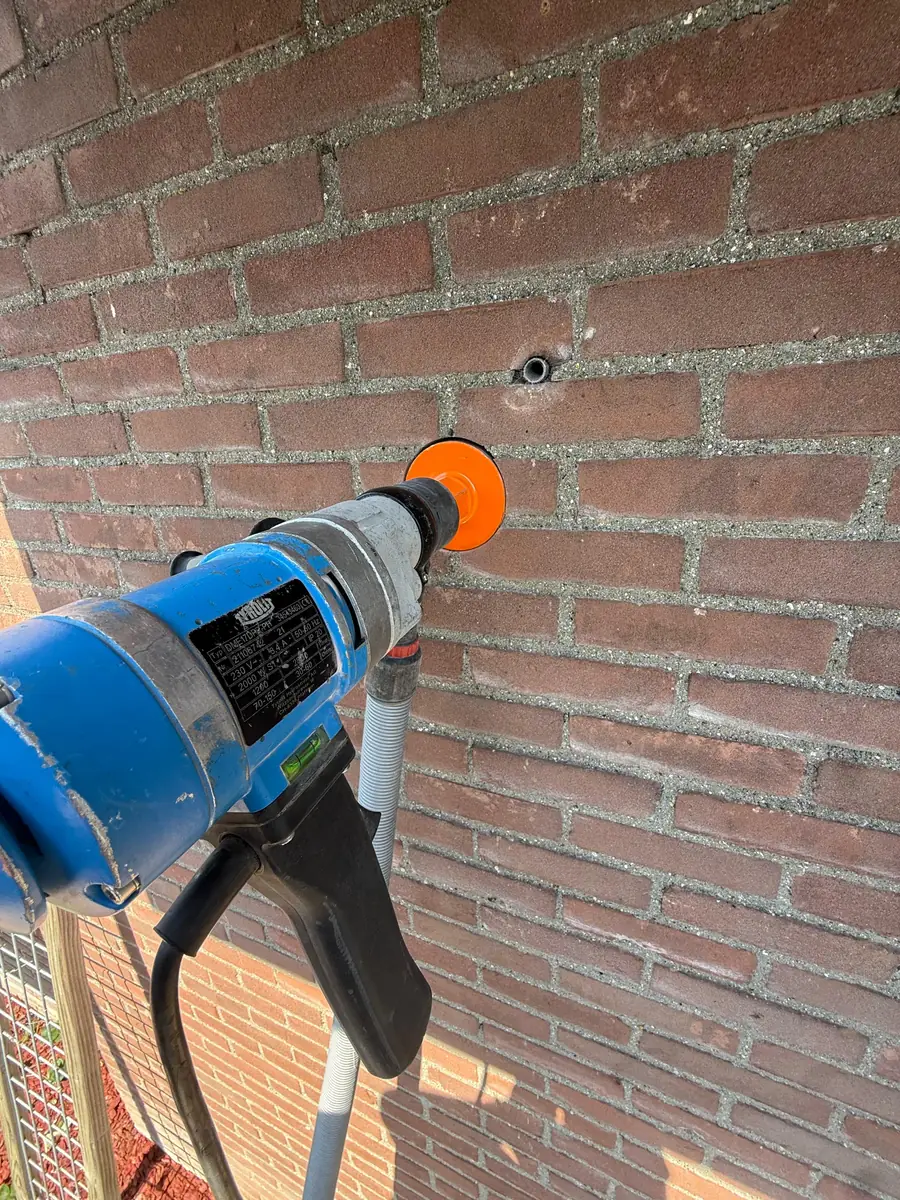 Betonboringen Peel en Maas &mdash; boren met een oranje diamantkroon in een gevel van rode baksteen
