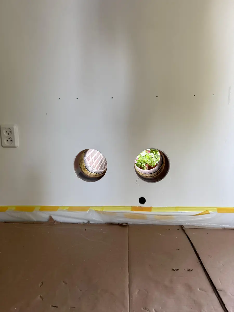 Betonboringen Uden &mdash; twee doorvoeren voor een monoblock-airco in een witte binnenmuur, met afgeplakte vloer