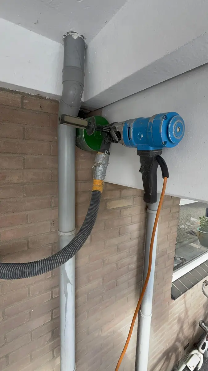 Betonboringen Venlo &mdash; boormachine hoog tegen de gevel naast de regenpijp, onder de dakrand