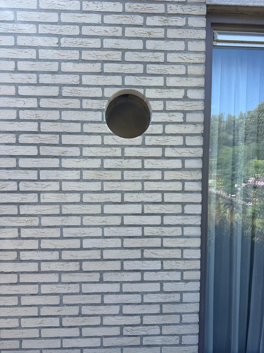Betonboringen Vught &mdash; ronde doorvoer in een gevel van witte baksteen naast een smal raam