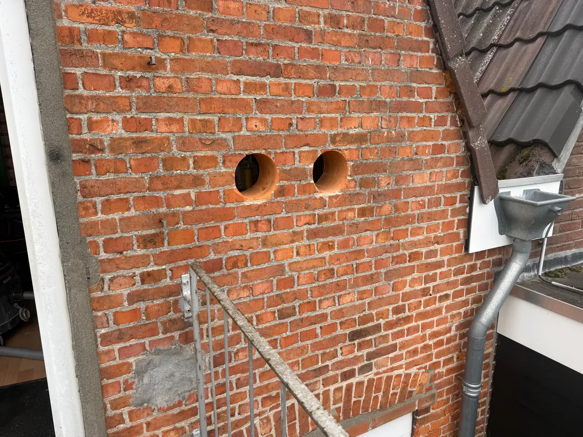 Betonboringen Woensdrecht &mdash; twee doorvoeren naast een buitentrap in een gevel van rode baksteen