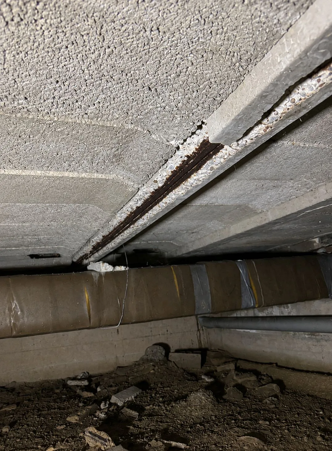 Betonrot aan de onderkant van een systeemvloer in de kruipruimte — afgebrokkeld beton en roestende wapening
