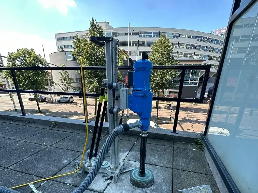 Diamantboormachine op een boorstatief op een dakterras, met de stofafzuiging aangesloten