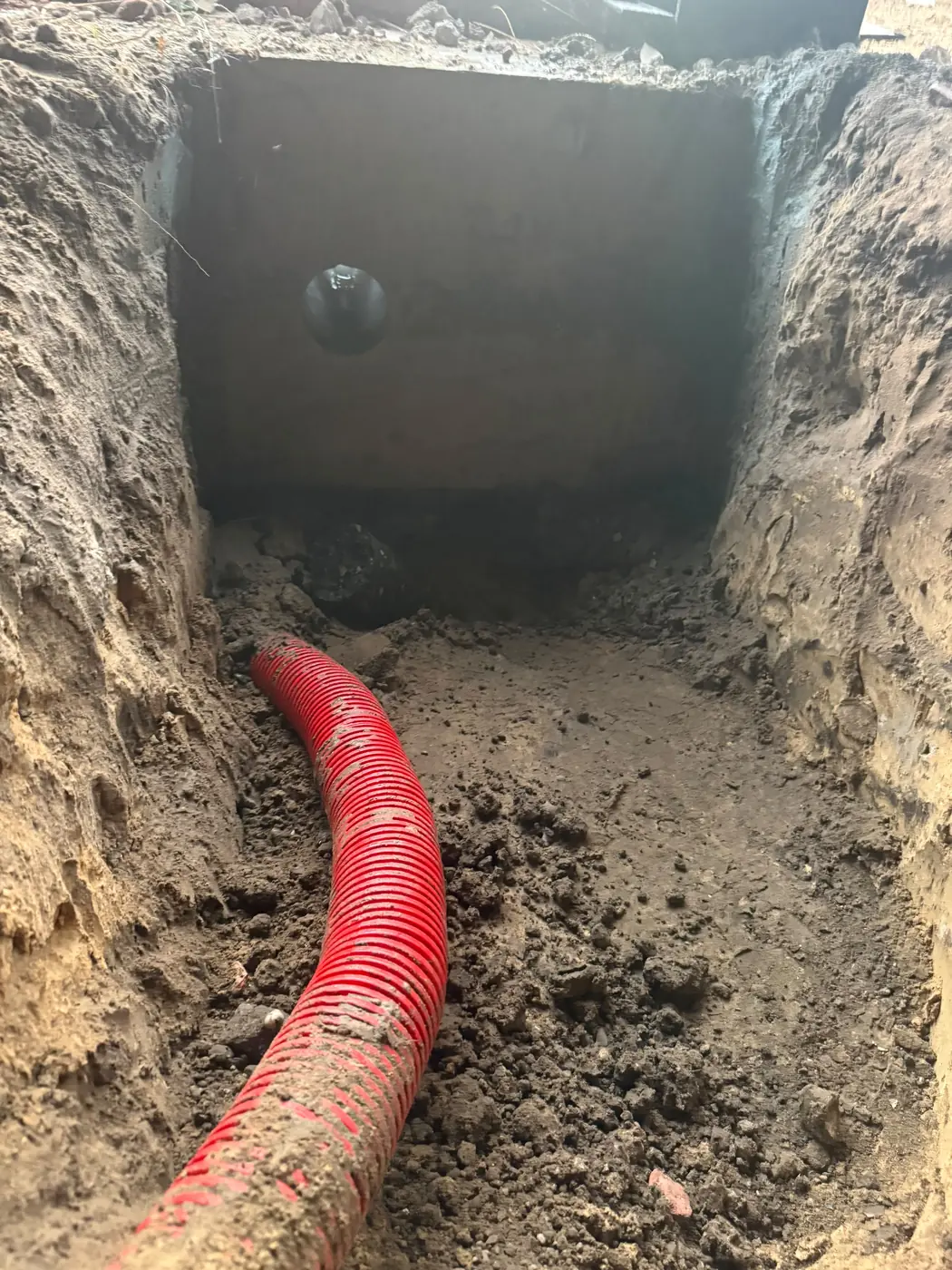 Ronde doorvoer van 132 mm in de funderingsbalk, met een rode mantelbuis in de sleuf ervoor