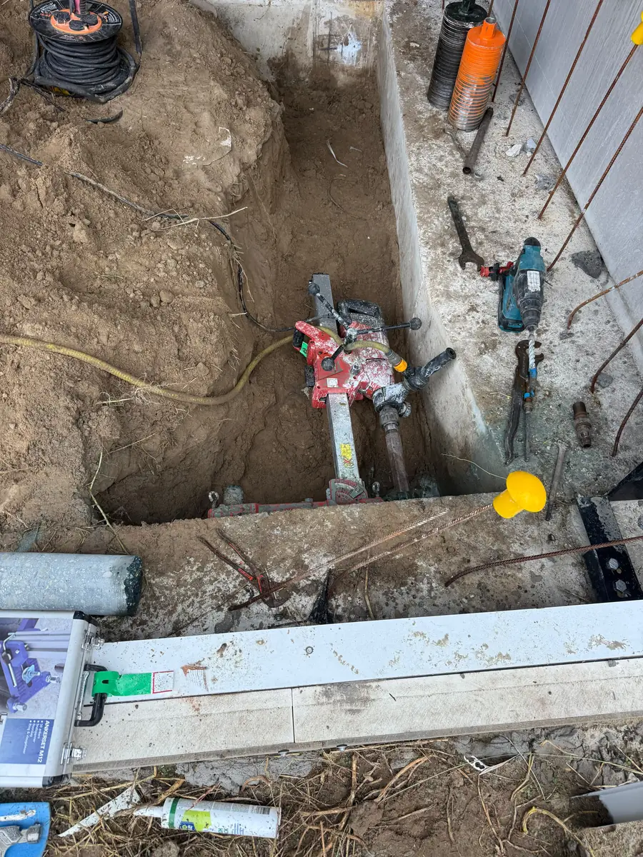 Hilti DD-150U op een boorstatief in de put tegen de funderingsbalk, met de watertoevoer aangesloten