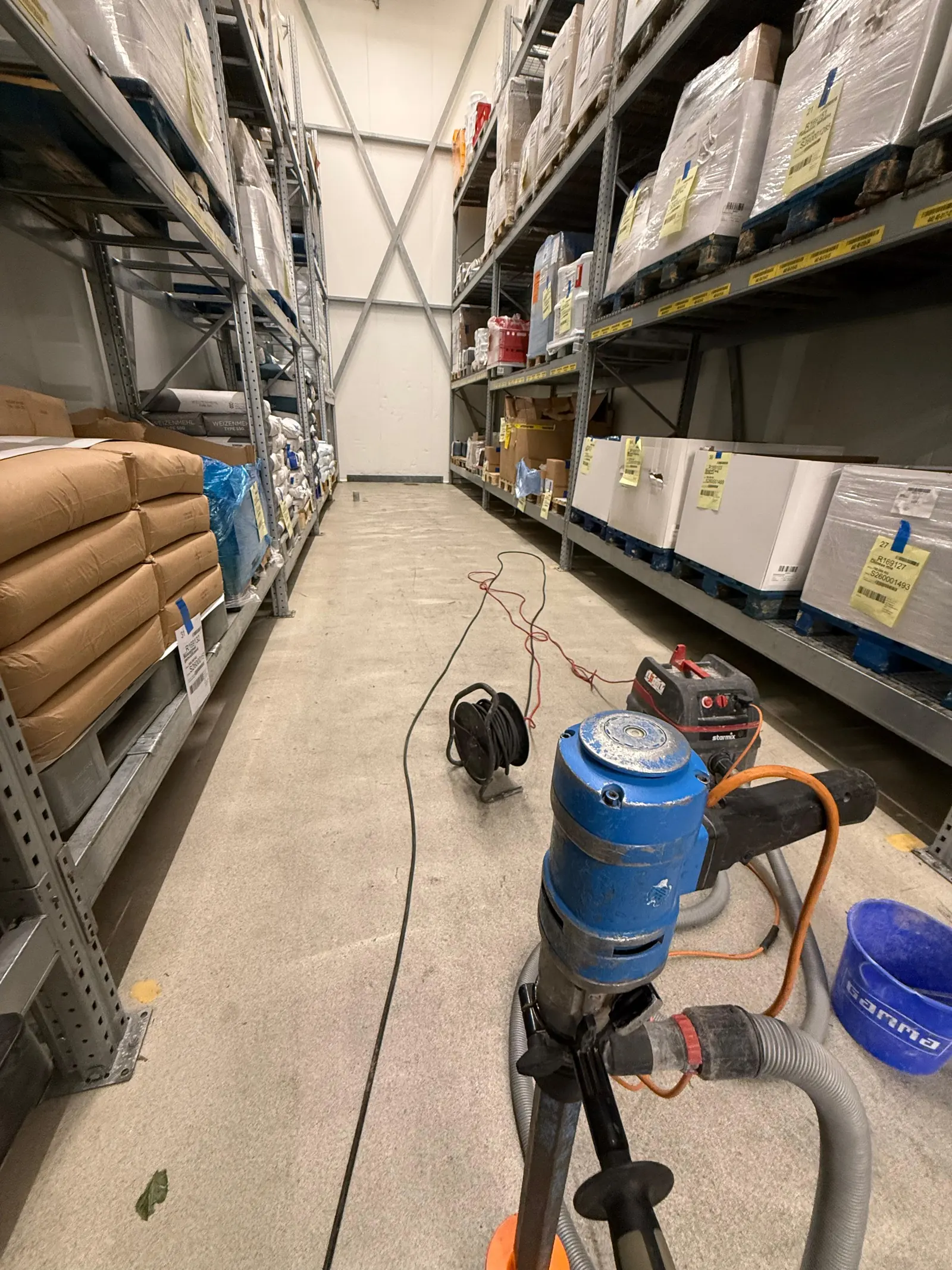 Boorstatief met diamantboormachine en stofzuiger in het grondstoffenmagazijn van Bonfait, tussen de stellingen met bloem en verpakkingen