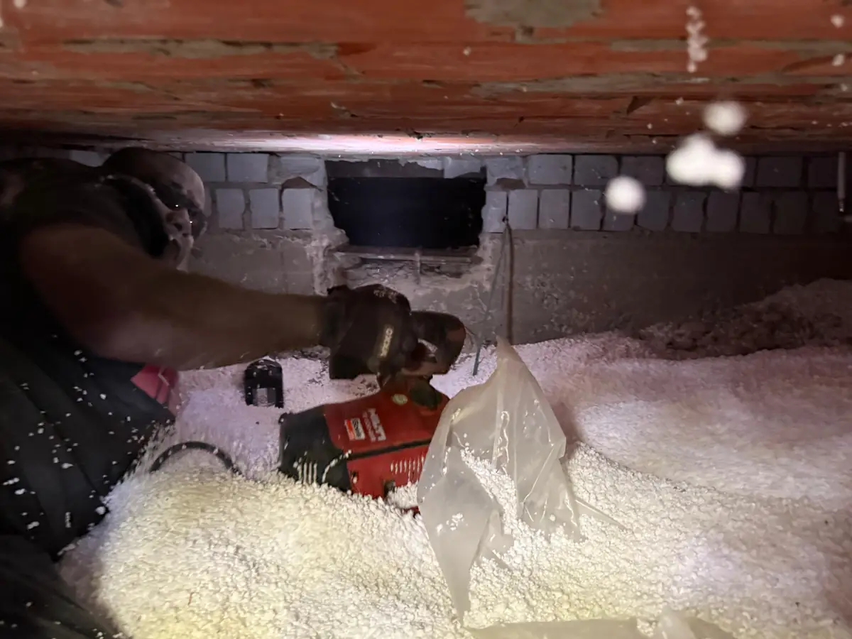 Kruipruimte met isolatieparels op de bodem en een opening in de tussenmuur