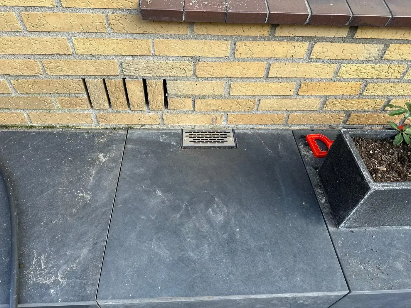 Ventilatierooster in donkere bestrating bij gele baksteenmuur