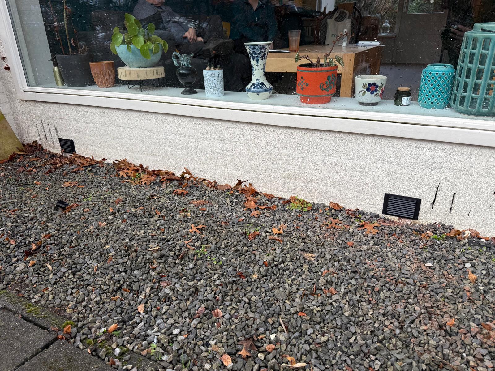 Twee ventilatiepunten in grindstrook bij witte gevel