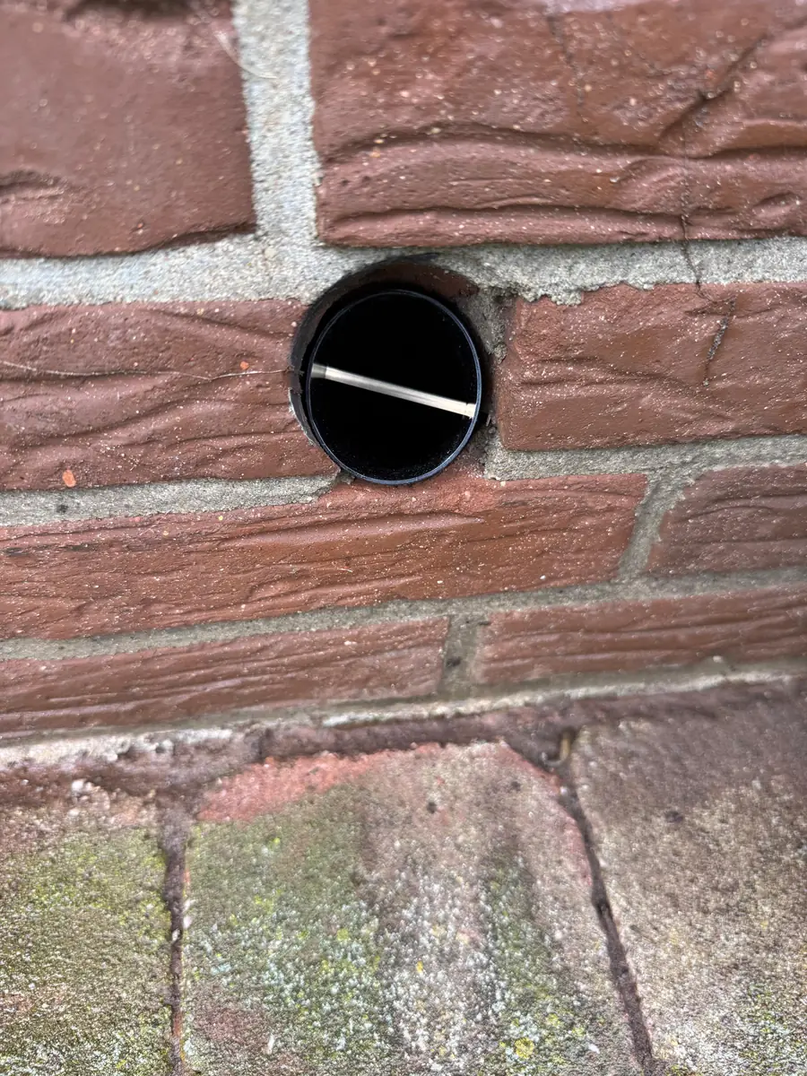Kruipruimte ventilatie Breda &mdash; Rond geboord ventilatiegat met koker in een rode bakstenen gevel