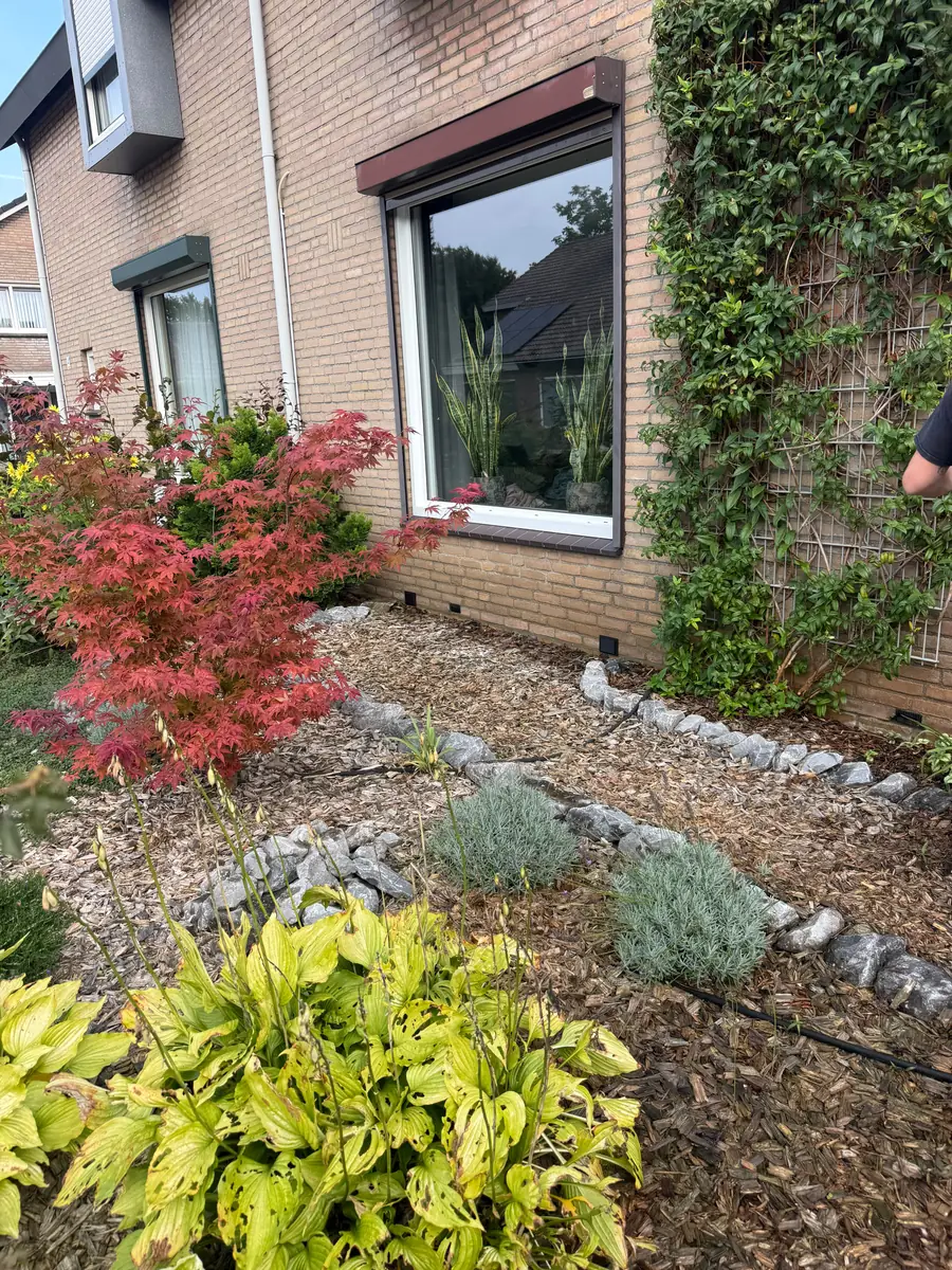 Kruipruimte ventilatie Meierijstad &mdash; Bakstenen gevel met een border van boomschors en keien, met het ventilatierooster onderaan de muur
