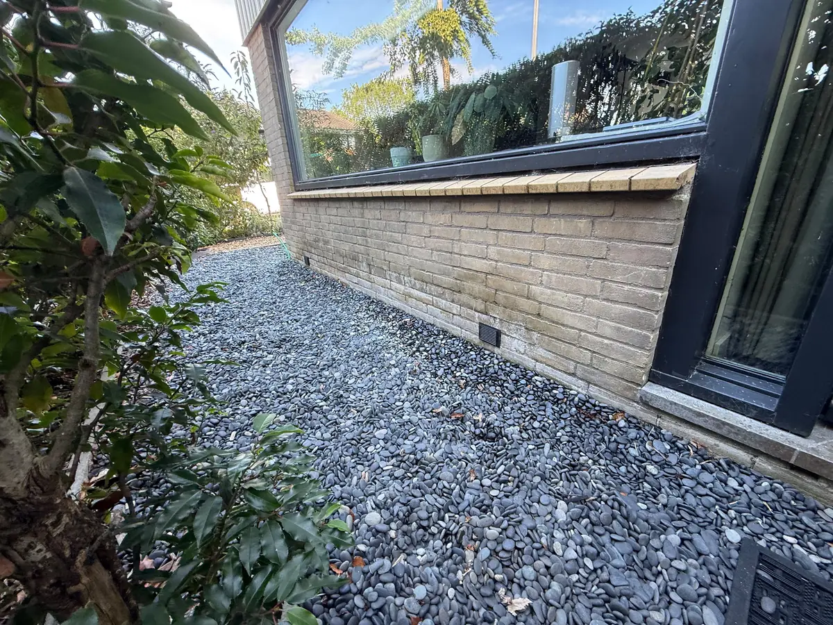 Kruipruimte ventilatie Maastricht &mdash; Ventilatierooster onderaan een lichte gevel langs een strook donker grind