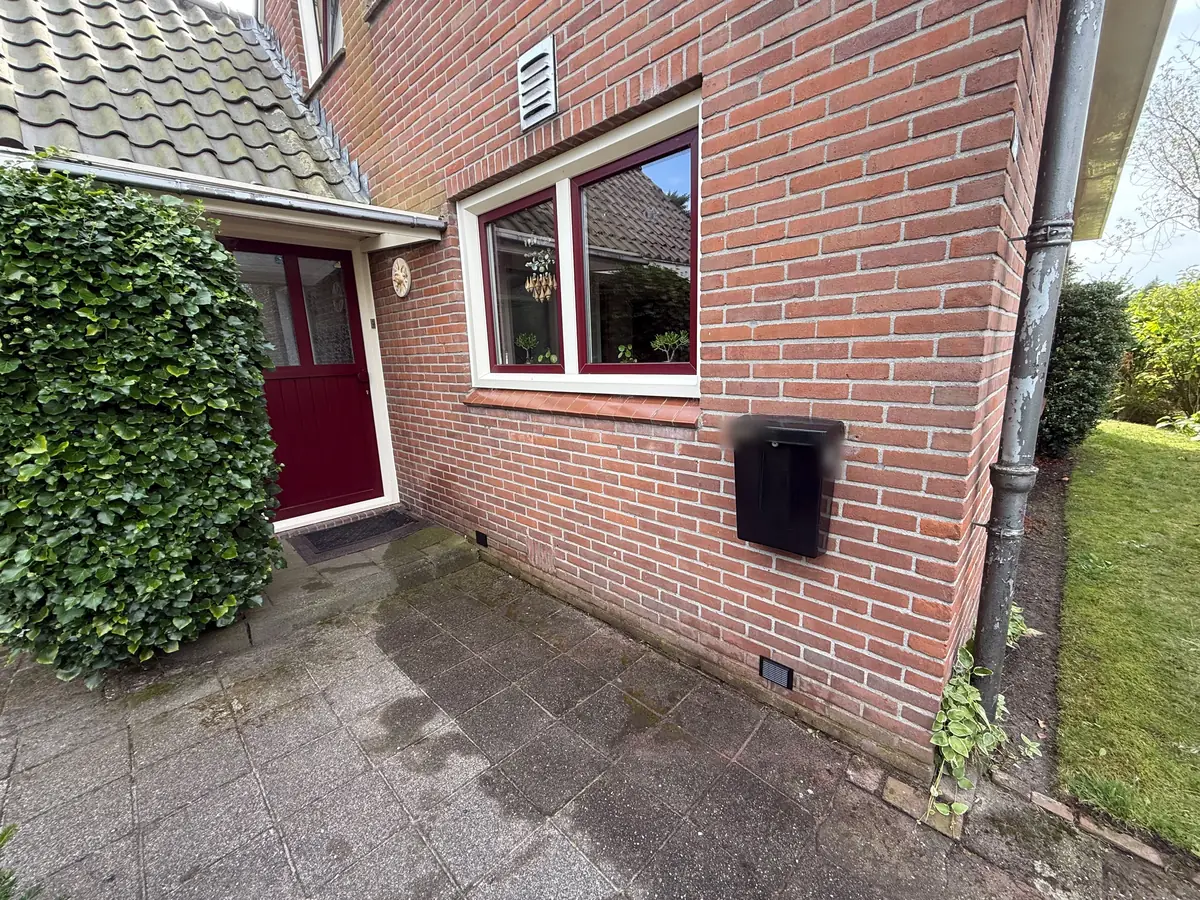 Kruipruimte ventilatie Bergen op Zoom &mdash; Klein zwart ventilatierooster onderaan de gevel, onder het raam naast een rode voordeur