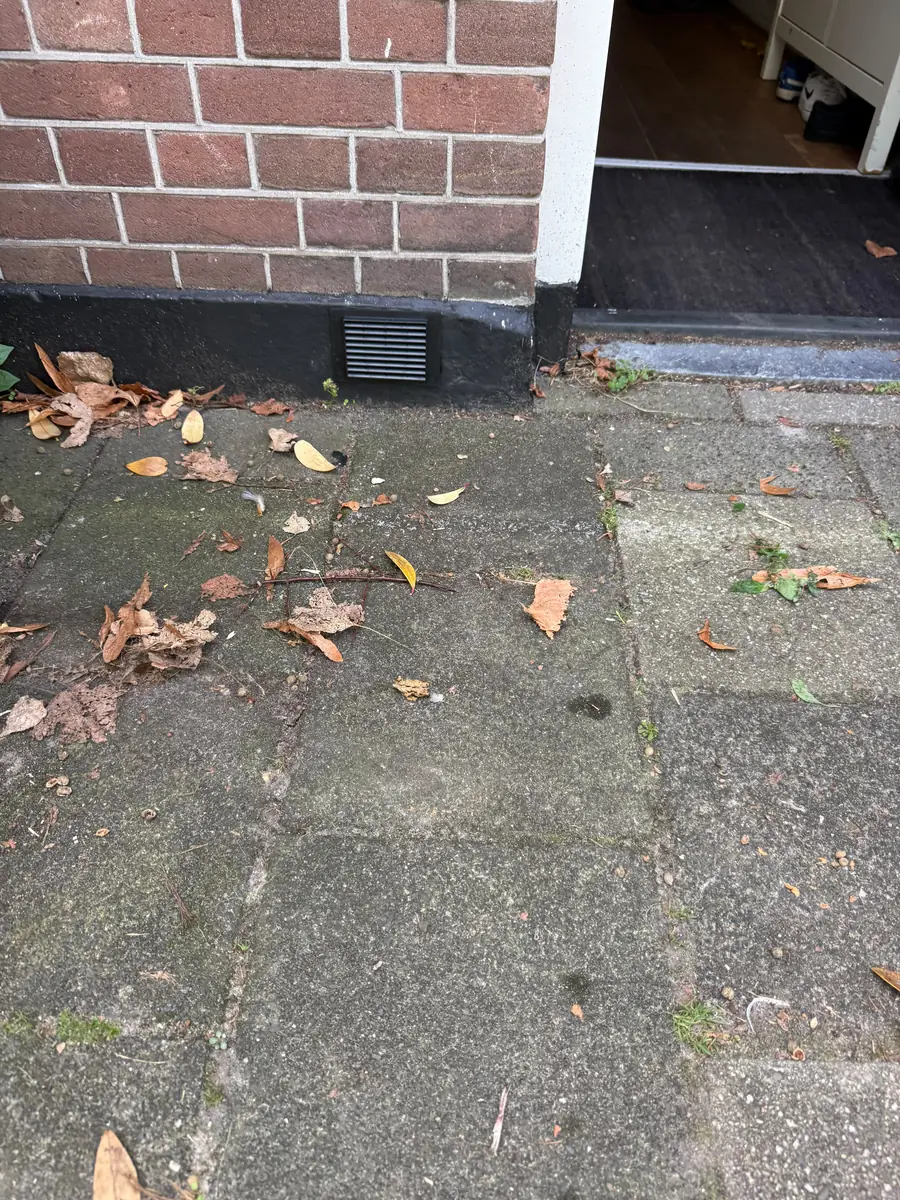 Kruipruimte ventilatie Roermond &mdash; Zwart ventilatierooster in de donkere plint naast een deur, boven de tegels