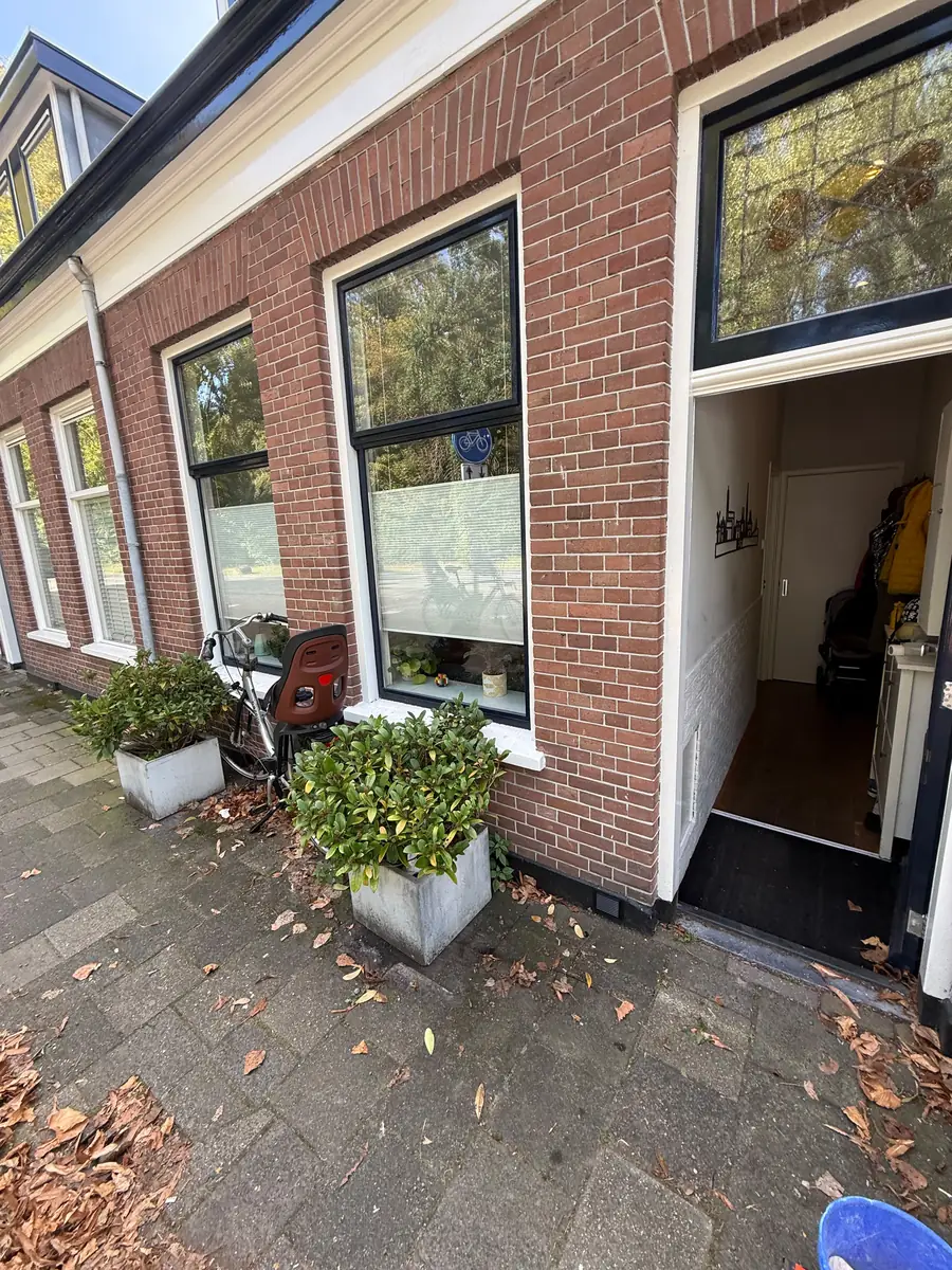 Kruipruimte ventilatie Bergen op Zoom &mdash; Bakstenen voorgevel met plantenbakken en een zwart ventilatierooster in de plint naast de voordeur