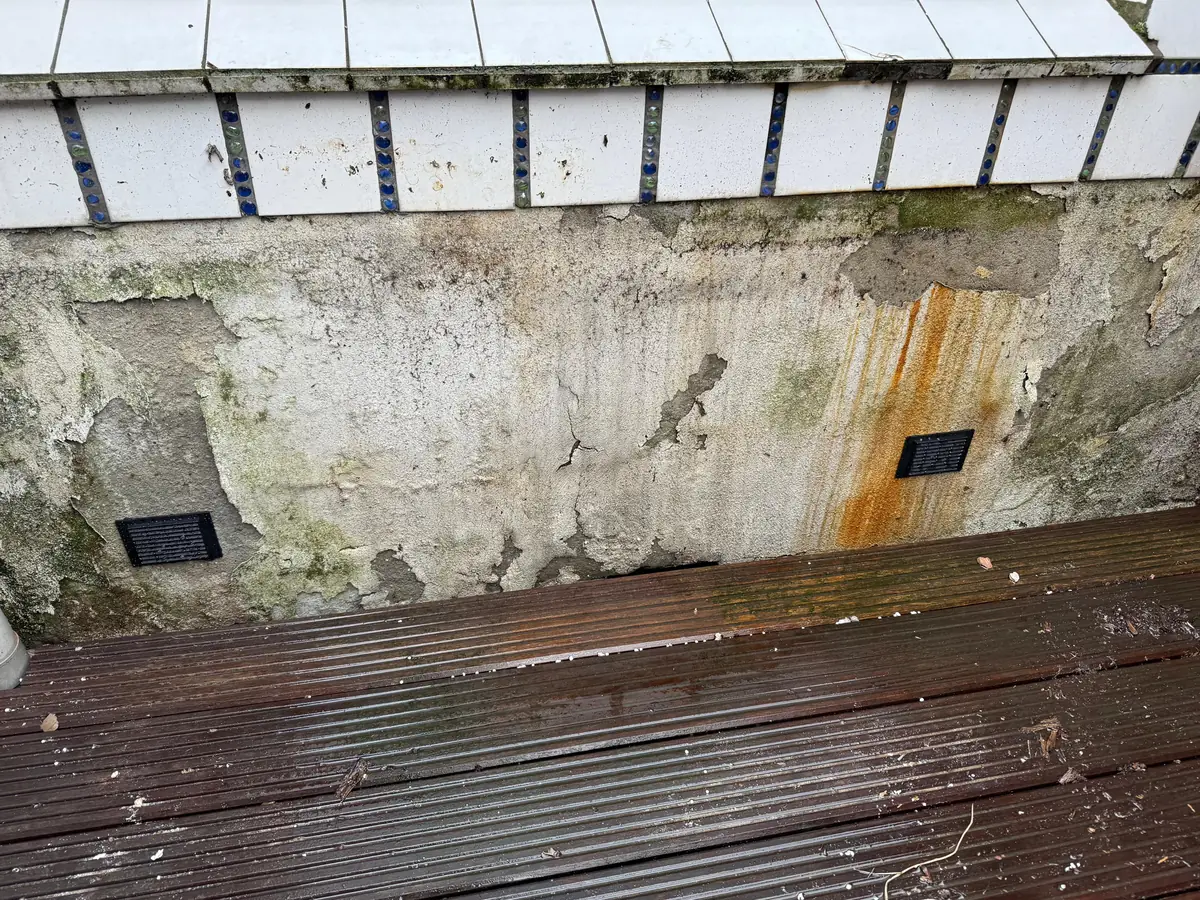 Kruipruimte ventilatie Kerkrade &mdash; Twee zwarte ventilatieroosters in een oude gepleisterde muur, boven een houten vlonder