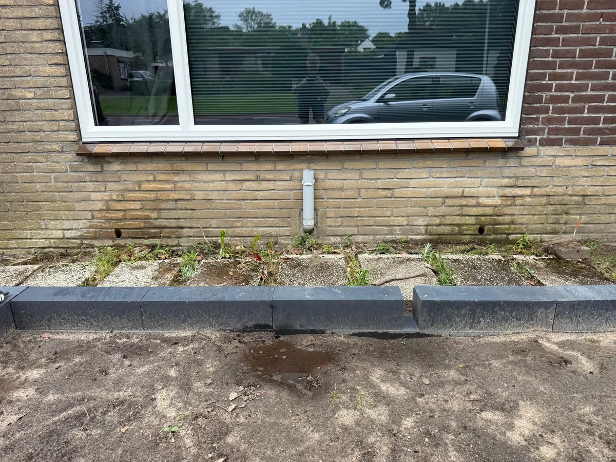 Kruipruimte ventilatie Veldhoven &mdash; Twee vers geboorde ventilatiegaten onder een raam, links en rechts van een witte afvoerbuis