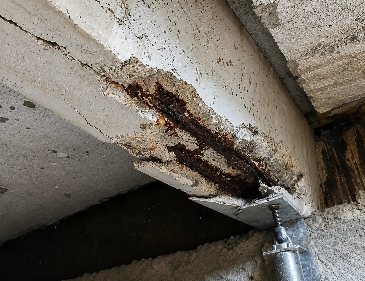 Betonrot in een mantavloer: afgespat beton met blootliggende, roestende wapening in de kruipruimte