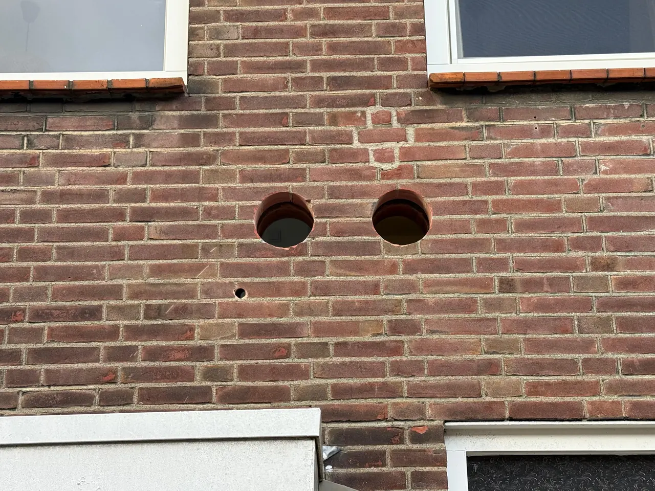 Twee monoblock airco doorvoeren op gelijke hoogte in de bakstenen gevel met een kleine condensboring eronder, geboord door Boorkoning