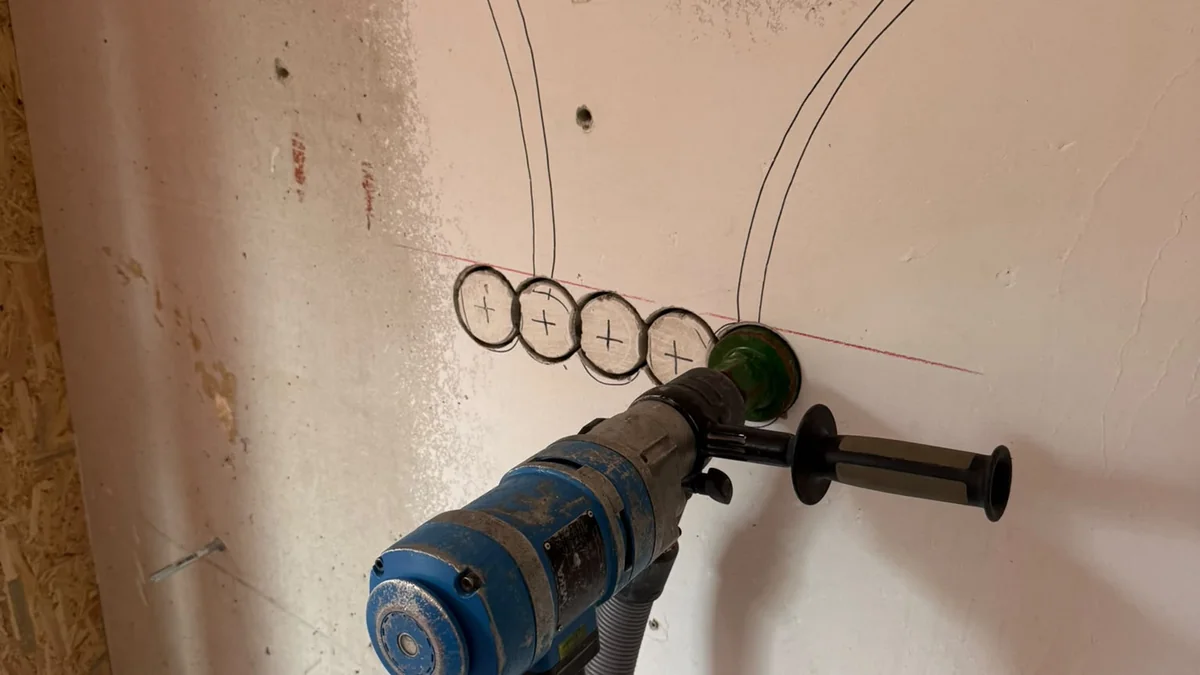 Inbouwdozen op een rij worden uitgeboord in een stenen muur, met de route van de kabels erboven afgetekend
